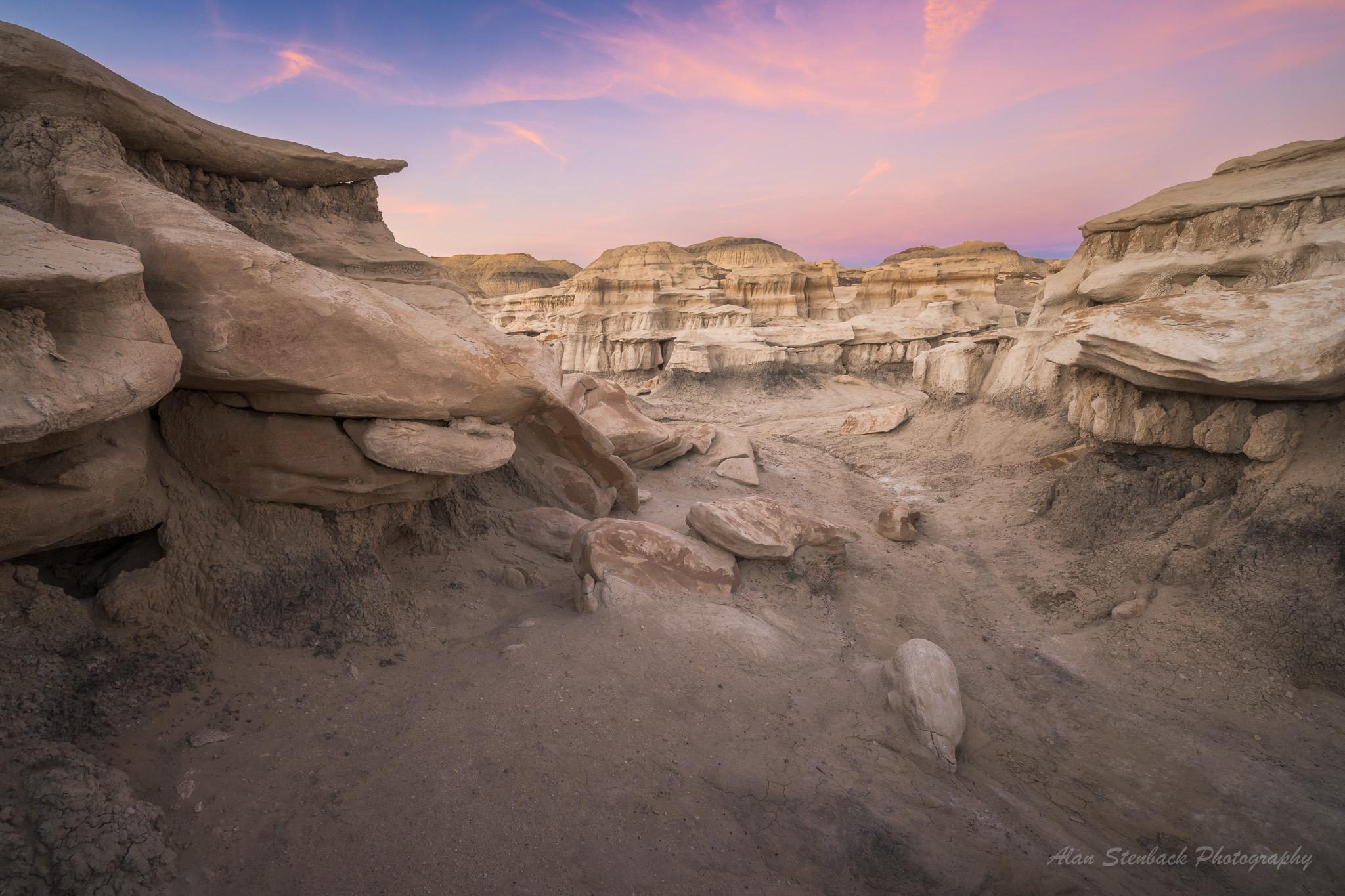 Bisti Badlands landscape with unique rock formations at sunset, featuring layered sedimentary rocks and a vibrant pink and purple sky.
