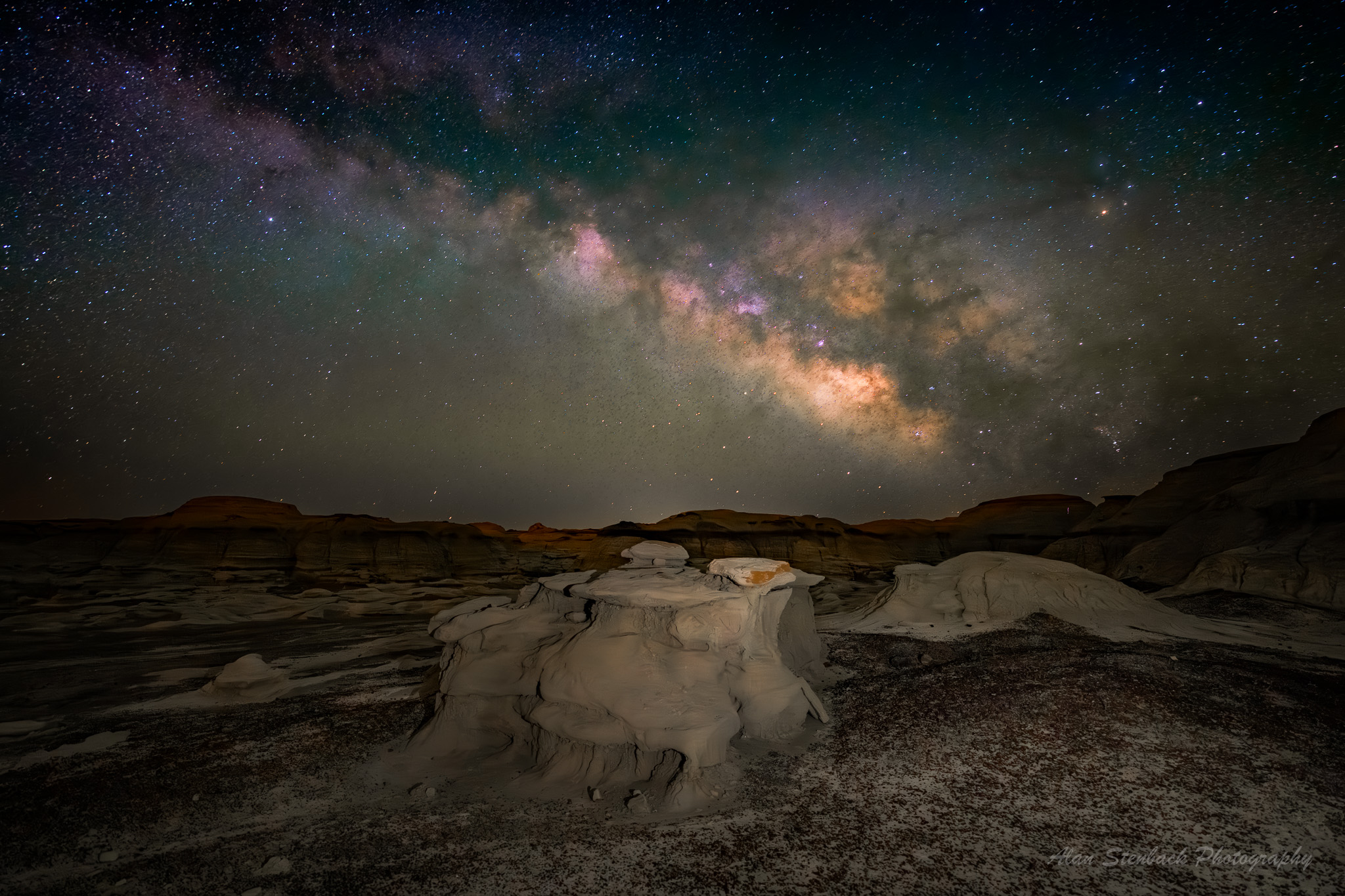 Night sky with vibrant Milky Way over desert rock formations, showcasing a stunning display of stars and cosmic colors.
