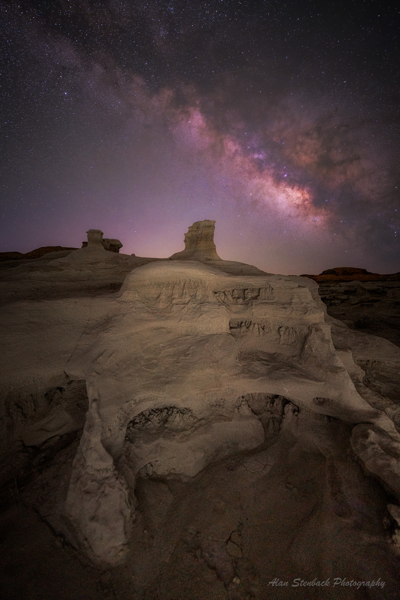 Dramatic rock formations under a vibrant Milky Way sky in a desert landscape at night.