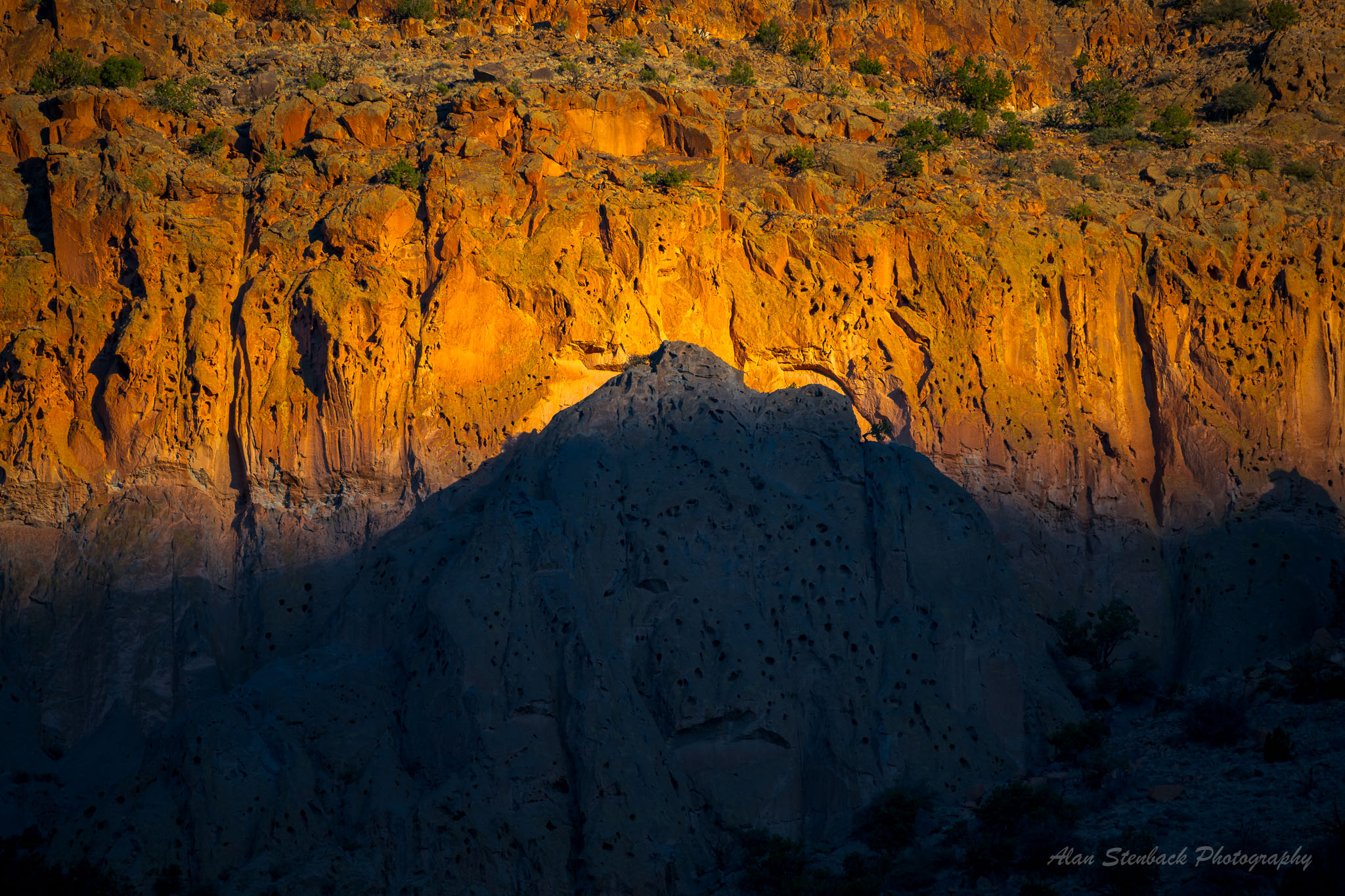 Sunset light casting dramatic shadows on Bandelier National Monument's cliff face.