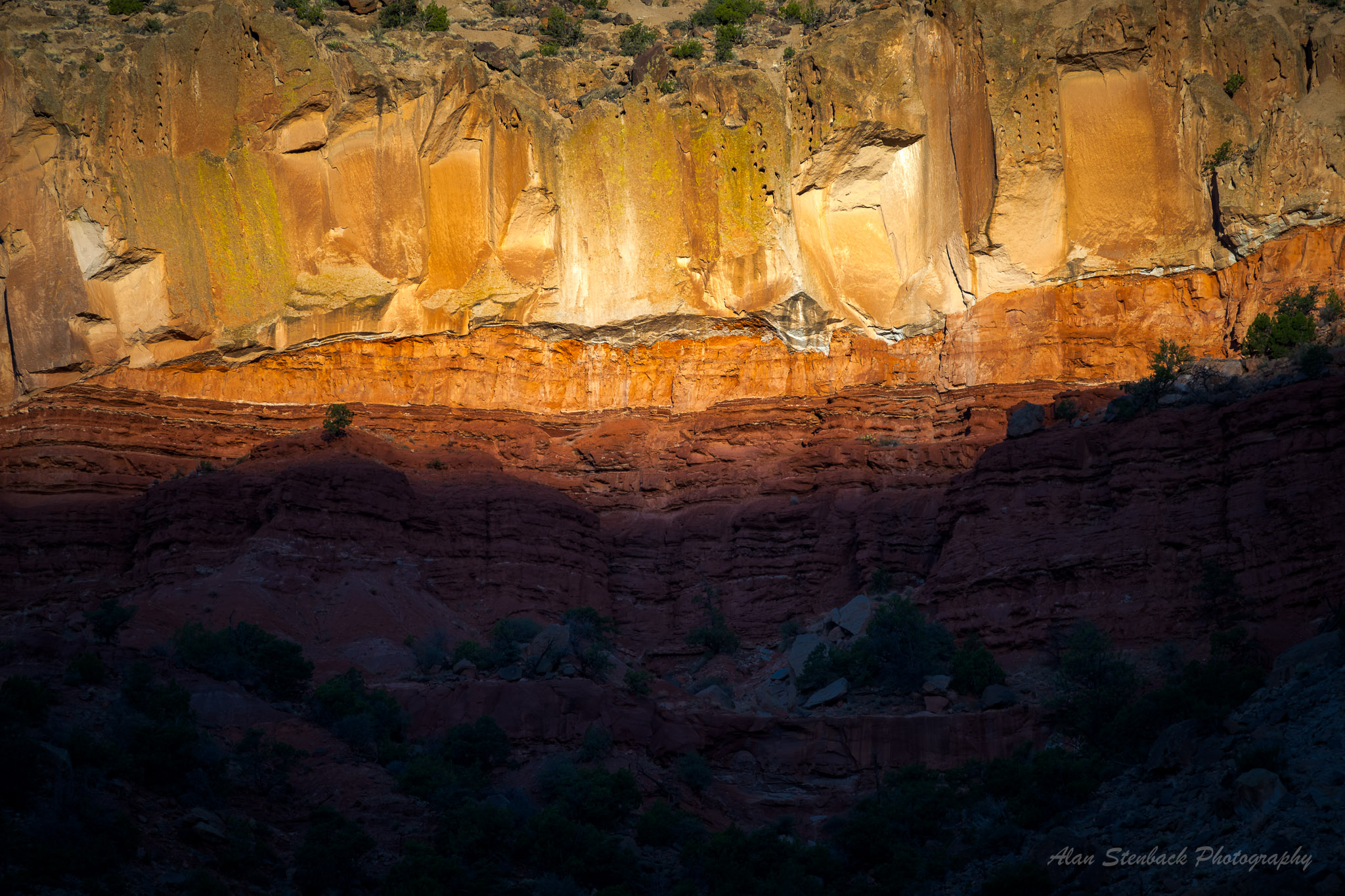 Striking red rock canyon wall with contrasting sunlight and shadow, highlighting textured layers of geology.