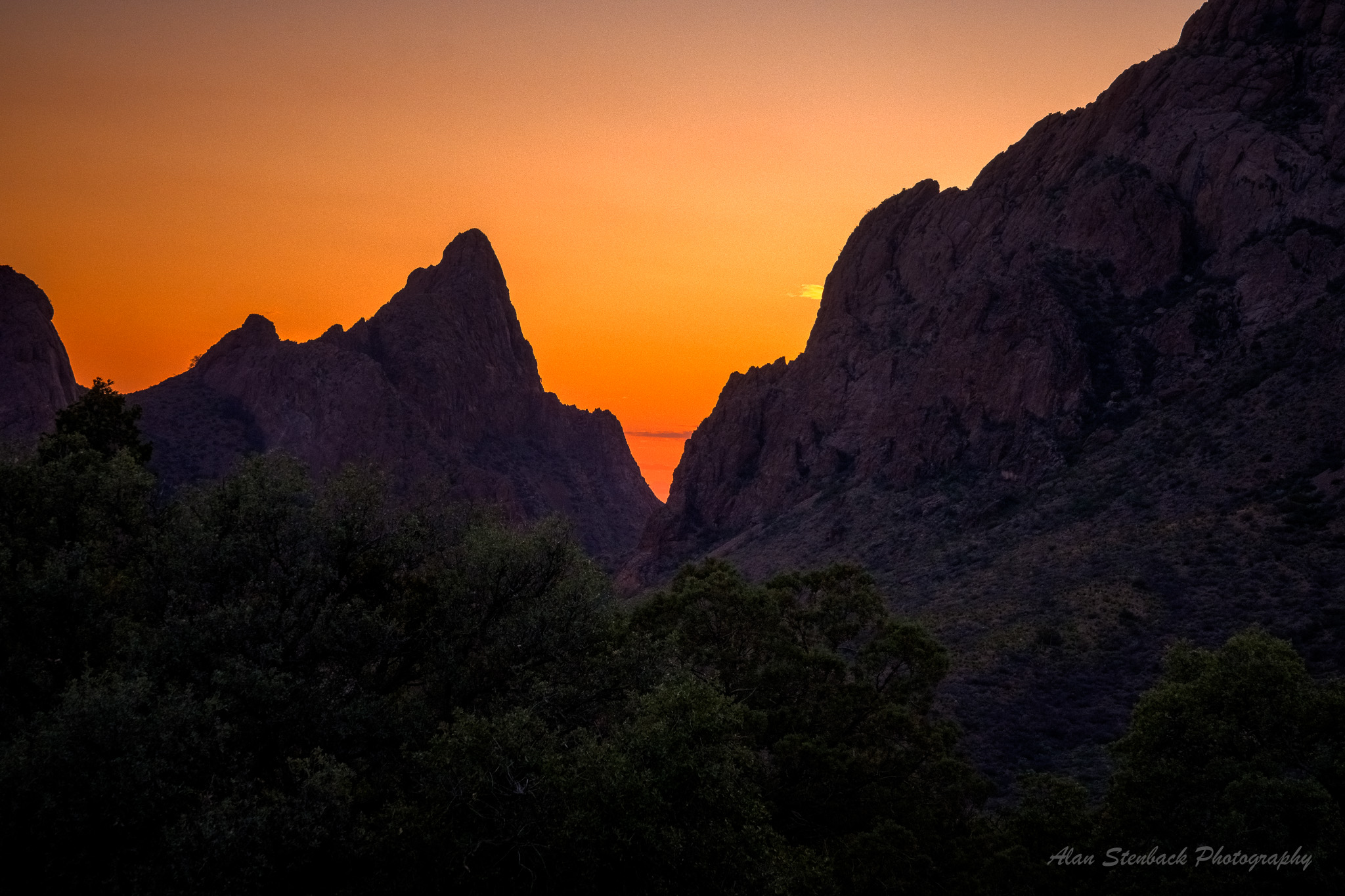 Sunset view of the Chisos Mountains' The Window in Big Bend National Park, Texas, with dramatic orange sky and rocky silhouette.