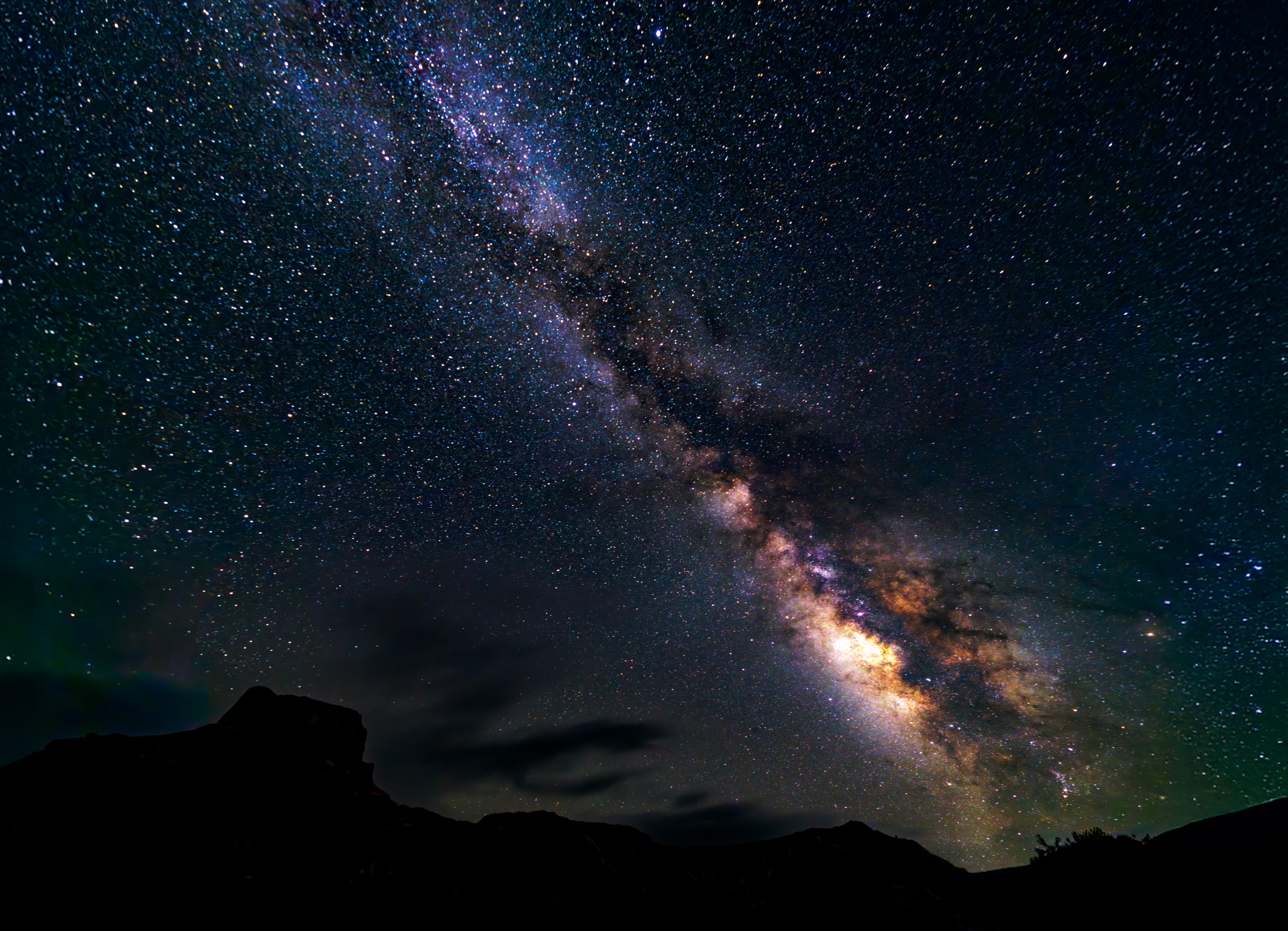 Milky Way galaxy stretching across a star-filled night sky above silhouetted mountains.