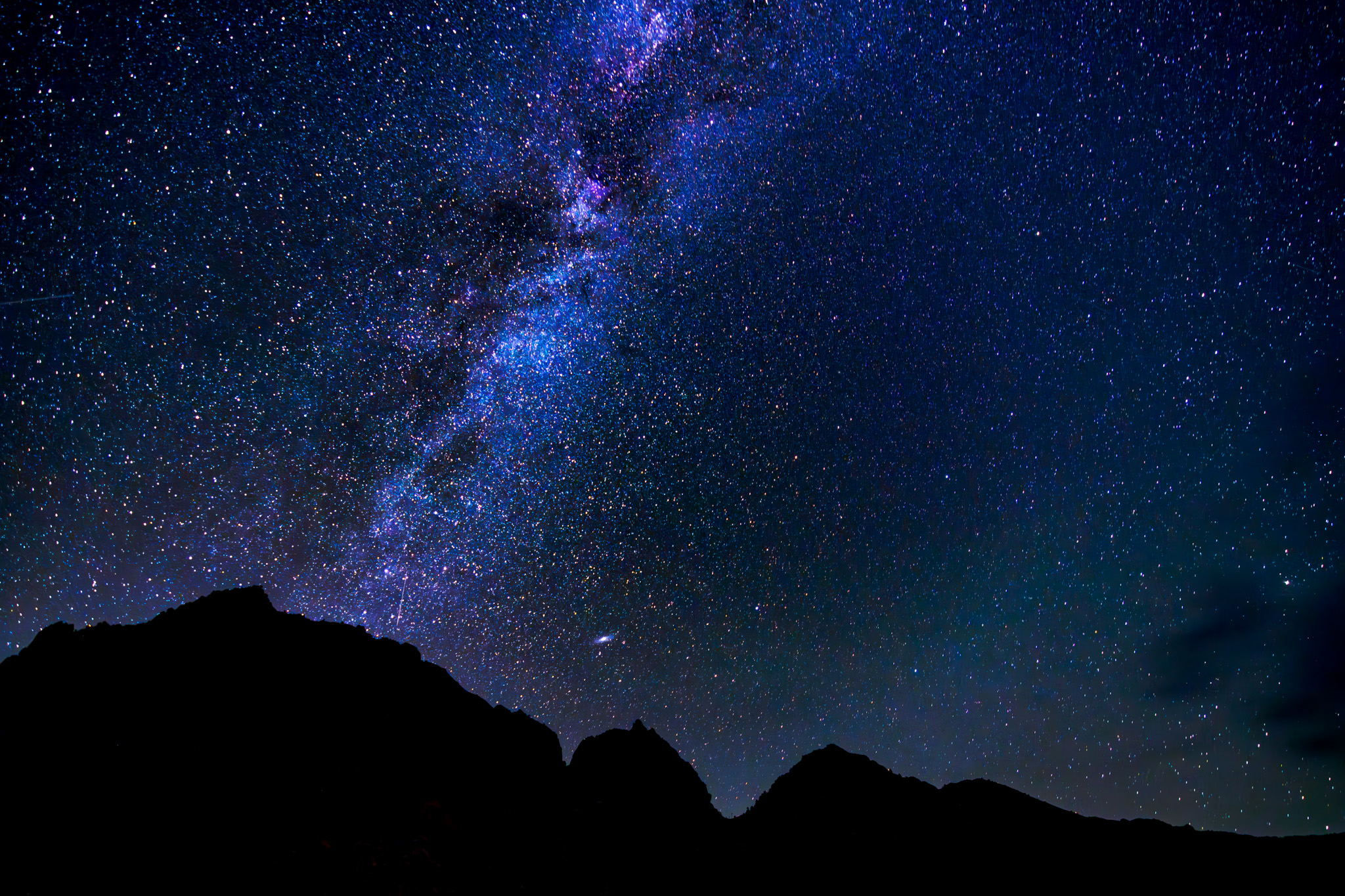 Starry night sky with Milky Way over silhouetted mountain peaks.