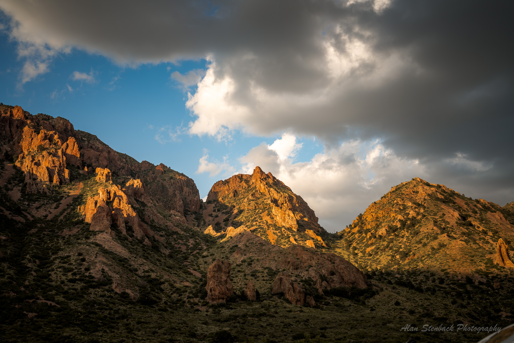 Sunlit rocky mountains under a dramatic cloudy sky, showcasing natural beauty and rugged terrain.