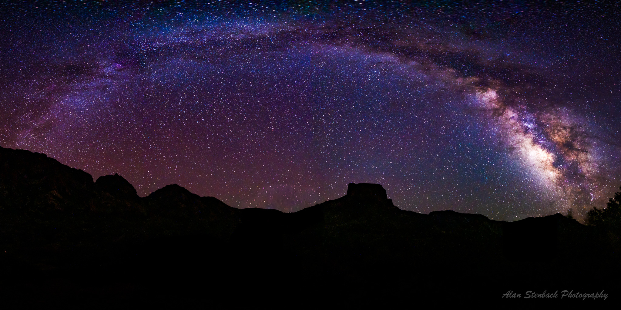 Milky Way galaxy arching over silhouetted mountain landscape during a clear starry night.